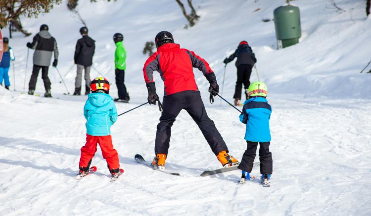 two small children on skis holding on to the ski poles of an adult on skis.