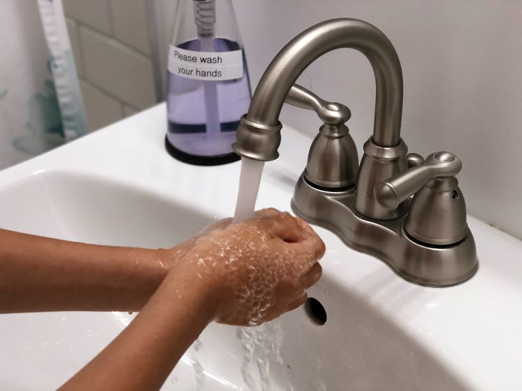 A person washing their hands under a faucet.