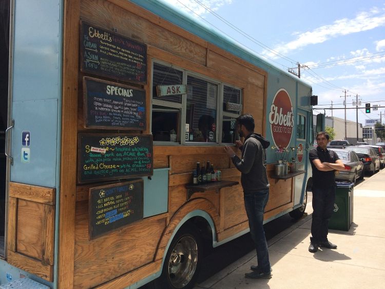 Two individuals standing outside a taco food truck parked curbside.