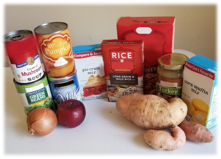 Various canned and boxed foodstuffs with produce such as potatoes and onions, sitting on a white counter.