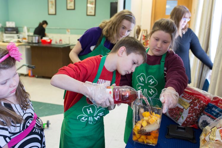 Youth pouring juice into a container of fruit.