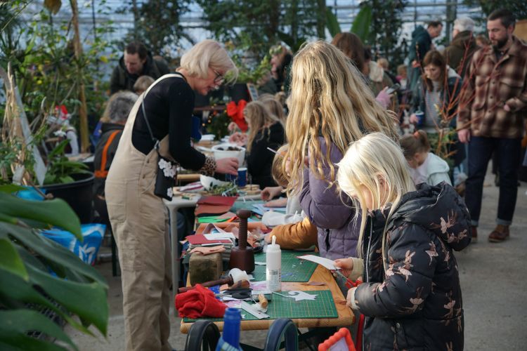 A volunteer helping a group of youth with craft projects in a greenhouse setting.