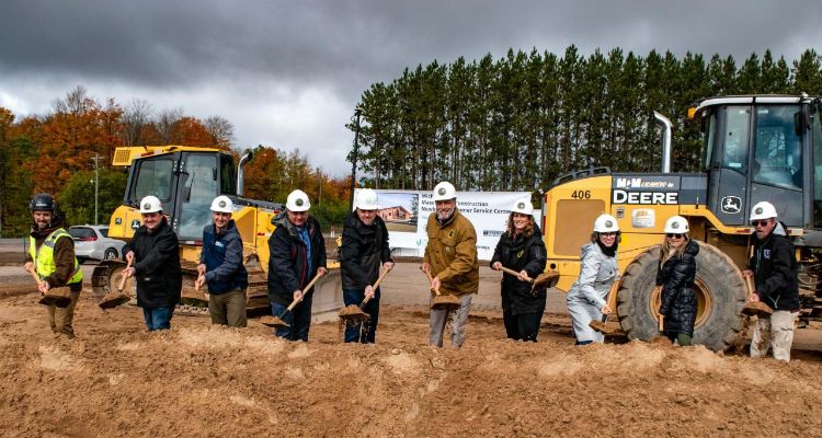 People on a construction site holding shovels in front of tractors.