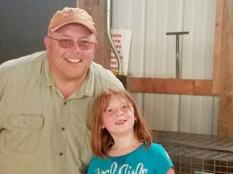 Daniel Lumm in a khaki shirt and orange hat with his niece in a blue shirt in a barn.