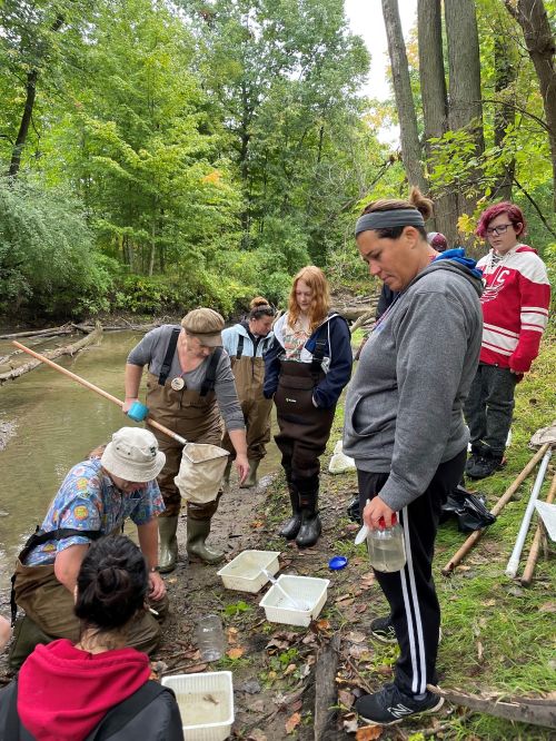 Youth and adults on the bank of a river looking at items from the river.