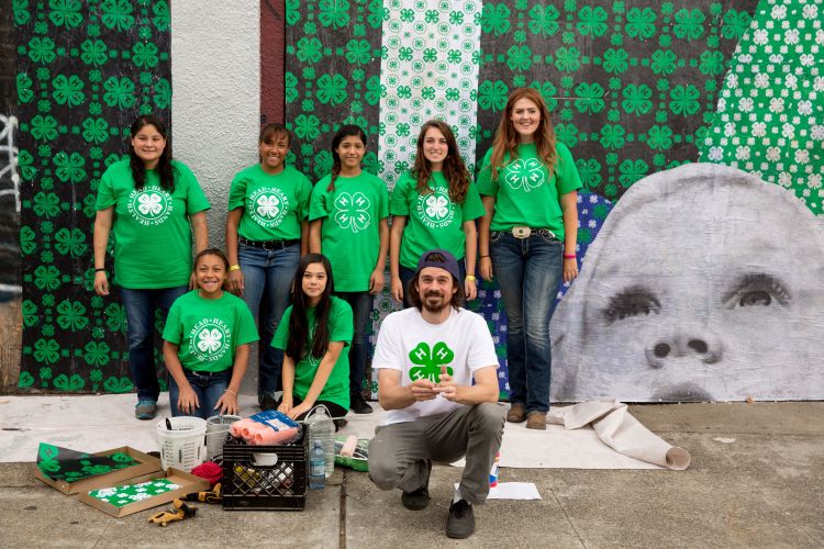 A 4-H group wearing green 4-H T-shirts in front of a 4-H wall mural.