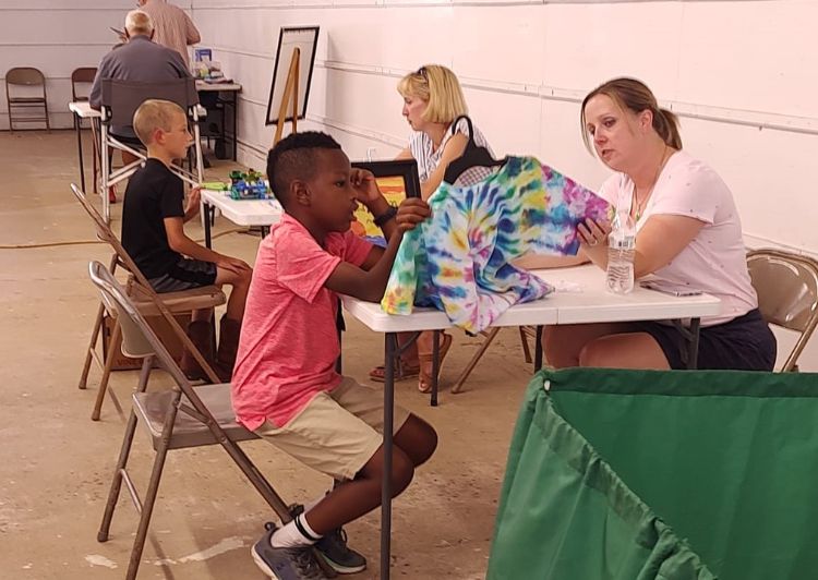 A young boy in a pink shirt sitting at a table with a woman looking at a blanket.