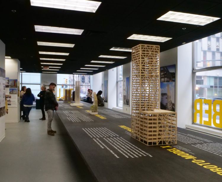 People standing around a wooden building model in an exhibit space.