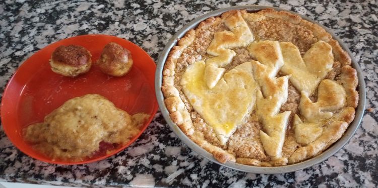 A red plate on with two small potatoes and one large spoon of food. On the right, a pie.