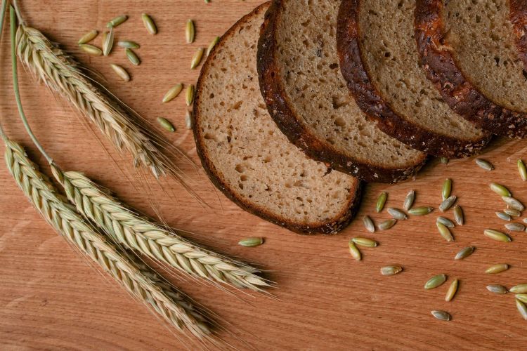 A photo of bread next to stalks of wheat and wheat seeds on a table.