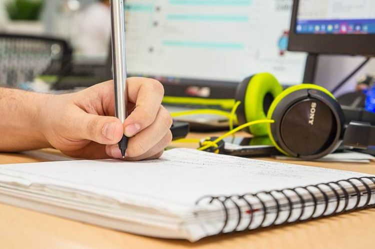 Hand holding a pen writing on a notebook