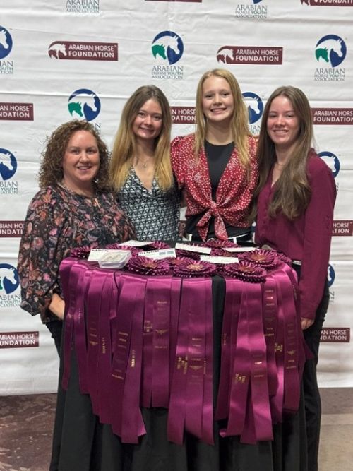 Three young girls and their female coach standing around a table with ribbons.