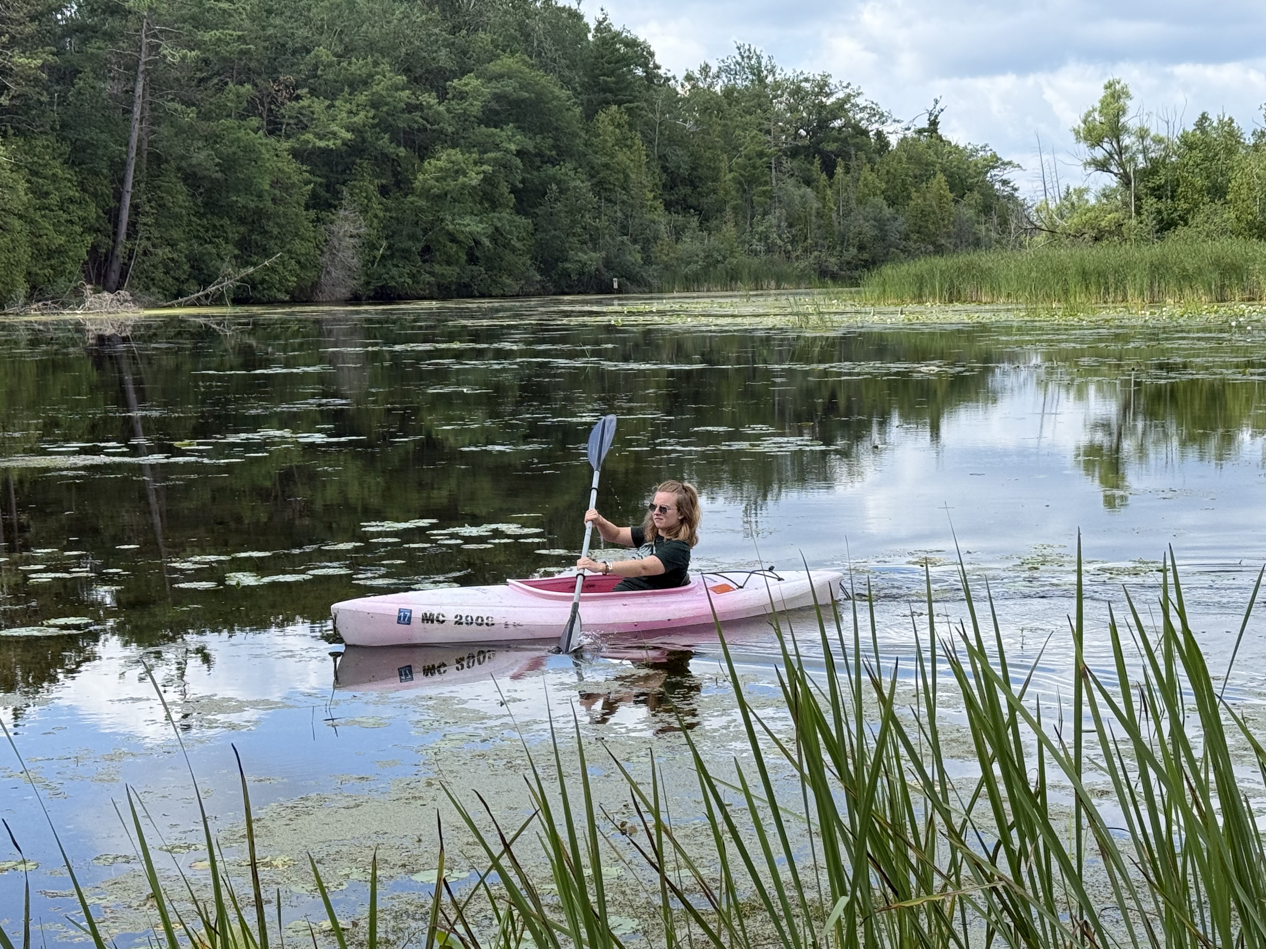 Woman paddles a pink kayak along a shore.