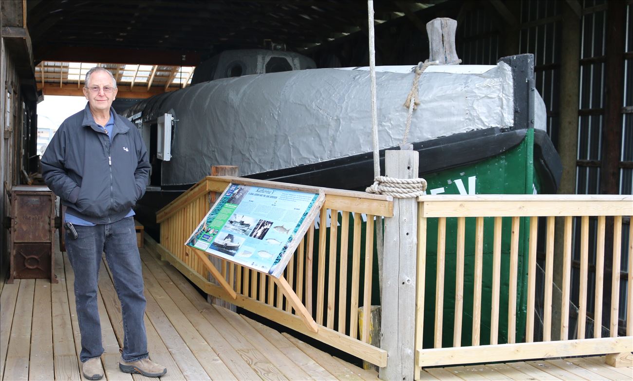man stands by an old boat that has been refurbished
